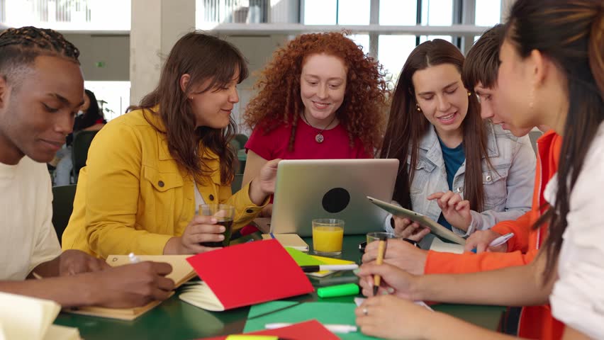 Diverse group of college students studying together at university cafeteria. Happy classmate friends talking while preparing exam or doing group work sitting on bar table outside. Education concept. | Shutterstock HD Video #1102739653