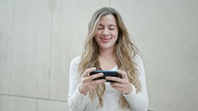 Young blonde woman smiling confident watching video onsmartphone at street