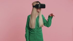Pretty caucasian young woman using headset helmet app to play realistic simulation games. Watching virtual reality 3D 360 video. Teenager girl in VR goggles gadget isolated on pink background, indoors