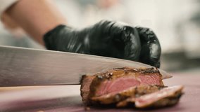 Process of cutting the steak with a large kitchen knife on a cutting board. The juicy beef meat is cut into pieces. Close-up of the chef's hand, slow motion. 4k footage