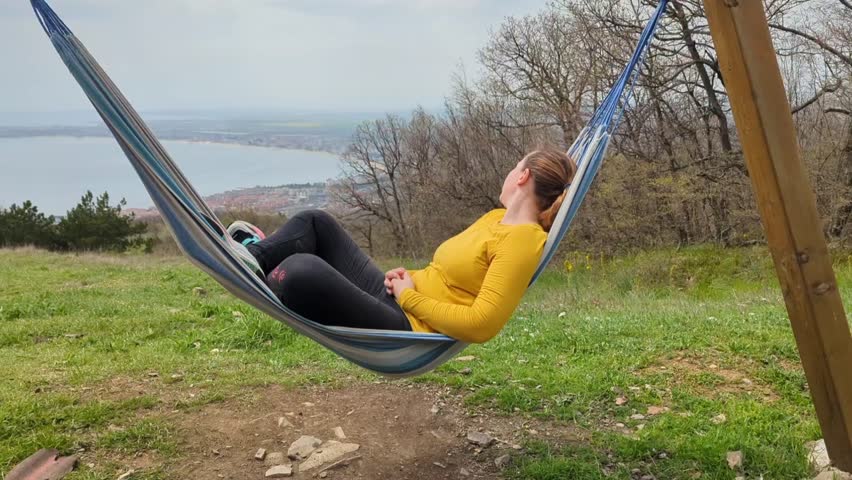 Woman resting in a hammock suspended high in the mountains, early spring around green grass and flowers
