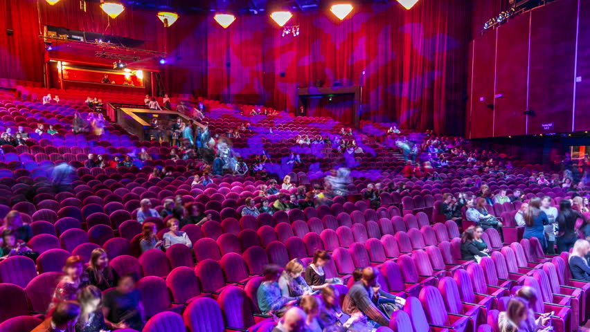Spectators gather in the auditorium and watch the show in theatre timelapse. Large hall with red armchairs seats. Viewers filling places until turn off the light. View from left side Royalty-Free Stock Footage #1102757111