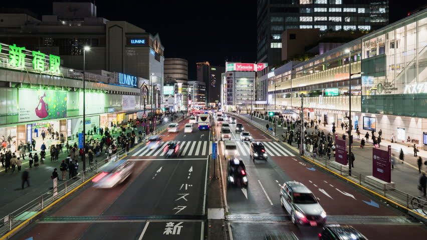 Tokyo, Japan - Dec 2, 2022: Time lapse of car traffic transportation, Japanese people, crowd Asian commuter walk cross road at JR Shinjuku subway train station. Asia transport, urban city night life