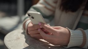 Closeup female hands typing by cellphone outdoors. Cheerful teenage girl sitting using smartphone in urban background. Social media, messenger, mob app, watching video, online shopping, browsing