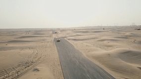 A yellow car is driving along an asphalt road in the desert, raising sand dust behind it. Drone Video