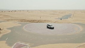 The car is parked in the middle of a roundabout on a road covered with sand in desert . Drone Video
