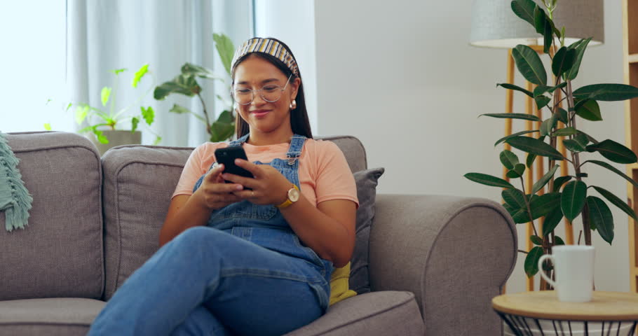 Asian woman, phone and relax on living room sofa for social media, texting or communication at home. Happy female relaxing on lounge couch browsing, scrolling or chatting on mobile smartphone indoors