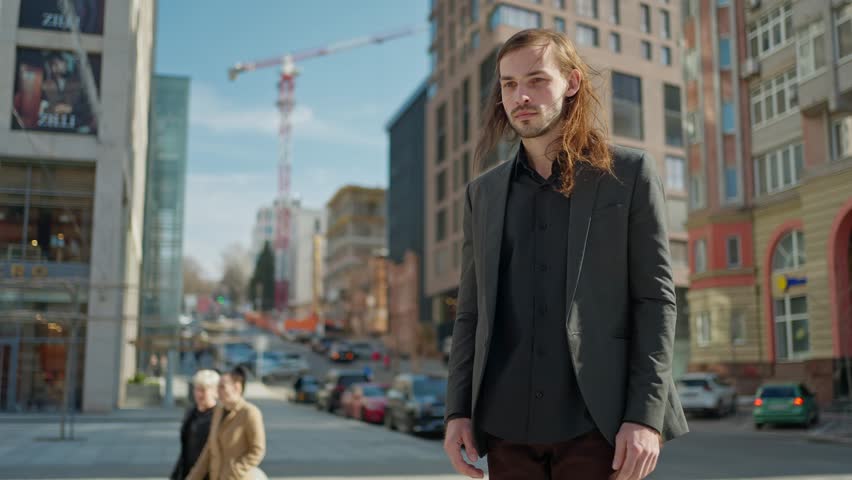 Portrait handsome man in coat looking at camera stand outdoors on background stairs. Sunlight at city street. Slow motion