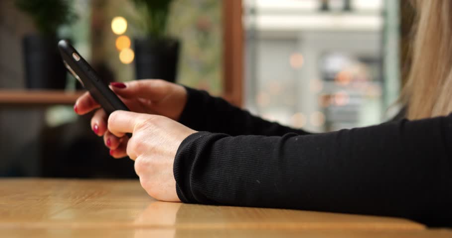 Unrecognizable young woman put blocked smartphone on table in urban coffee shop. Anonymous female with long hair turns off mobile phone and puts it aside on wooden table. High quality 4k footage