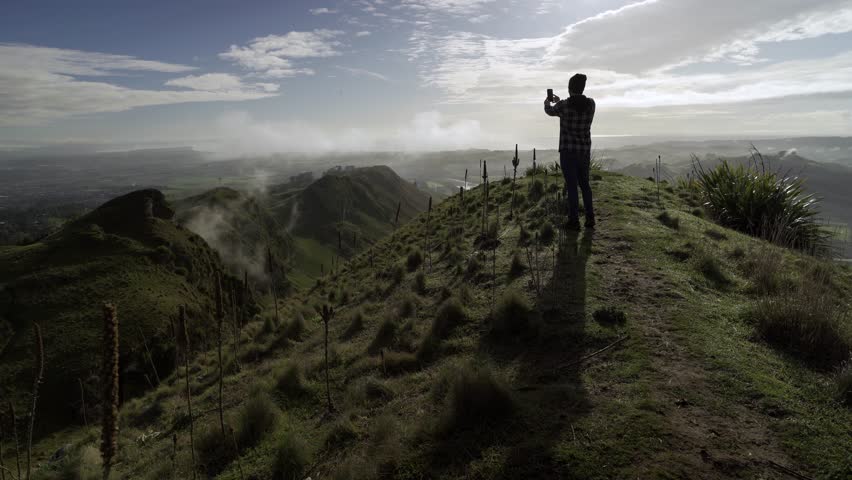 Young man walking on the trail of a mountain and taking photos and selfie. 4k video