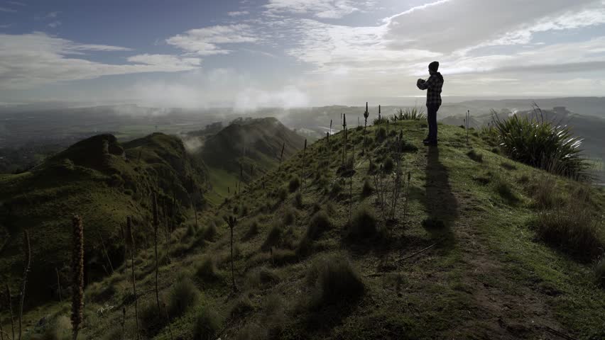 Man taking photos with a camera on the peak of a mountain on a foggy morning. Te Mata Peak, Hawke