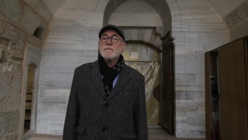 Old man in a hat visiting the interior of the historical mosque, muslim man visiting the ottoman mosque made of stone