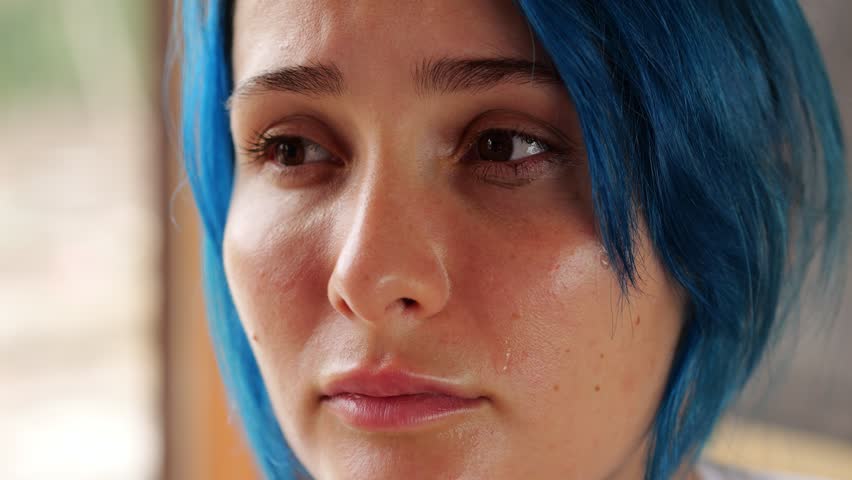 Very close portrait of face of young weeping woman, tears coming from her eyes. Woman have blue dyed hair, look aside and emotionally move lips. She feel sorrow or bad because of some news or people Royalty-Free Stock Footage #1102788641