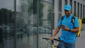 Portrait of the Happy African American Courier in Special Uniform Walking Near the Business Centre, Using Smartphone and Scrolling Customers Orders. Bicycle Delivery - Powered by Shutterstock - Get 15% off with code: PIKWIZARD15