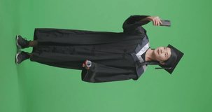 Full Body Of Asian Woman Student Graduates In Cap And Gown With Diploma Having A Video Call On Smartphone While Standing On The Green Screen Background In The Studio
