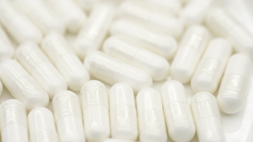 Production of pharmaceuticals and drugs, large number of capsules. White medical pills rotating closeup. Pills and drugs. Pharmaceutical Industry. The medicine concept.