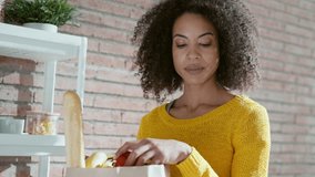 Video of happy beautiful woman holding cardboard bag with health shopping in kitchen at home