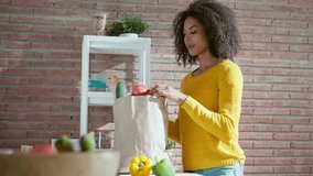 Video of happy beautiful woman holding cardboard bag with health shopping in kitchen at home