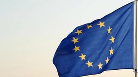 Flag of Europe or European Union Flag with twelve golden stars circle on a blue background, representing union of peoples of Europe. European union flag on pole waving in the wind on sky background - Powered by Shutterstock - Get 15% off with code: PIKWIZARD15