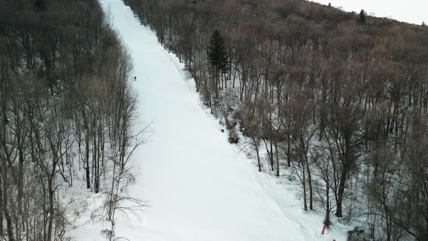 The aerial footage with slow zoom in captures the exciting movements of a snowboarder carving down the slopes of Yabuli resort, surrounded by stunning scenery. 