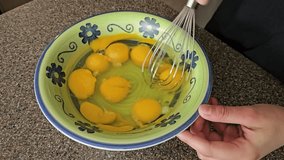 Breaking up egg yolks in food preparation bowl with wire wisk