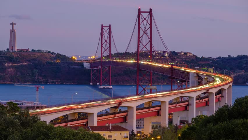 Time-lapse from Miradouro do Bairro do Alvito viewpoint of Tagus river, traffic on 25th of April Bridge and Christ the King statue in the evening twilight. Lisbon, Portugal. Zoom in effect