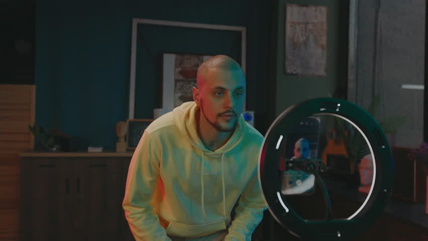 Influencer On Social Media. Cheerful Young Man Dancing In Front Of Camera. He Looks At Phone And Touches His Face.