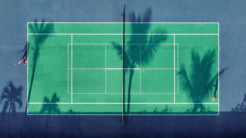 Aerial top down above people playing tennis. 4K drone of the tennis match. Athletic people practicing tennis at sunset time with scenic palm trees shadows on green field. Game players throwing ball 4K