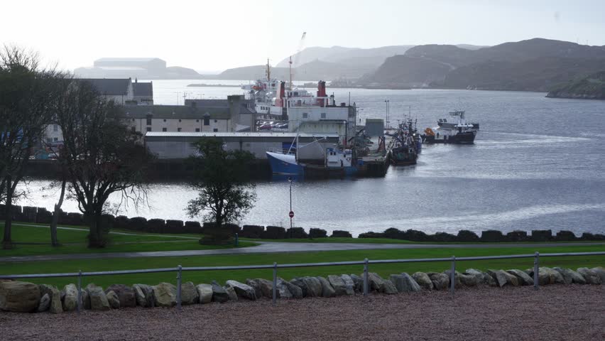 Shot of fishing boats moving around a harbour and pier. Various vessels are moored in port. Shot in Stornoway on the Isle of Lewis, part of the Outer Hebrides of Scotland.
