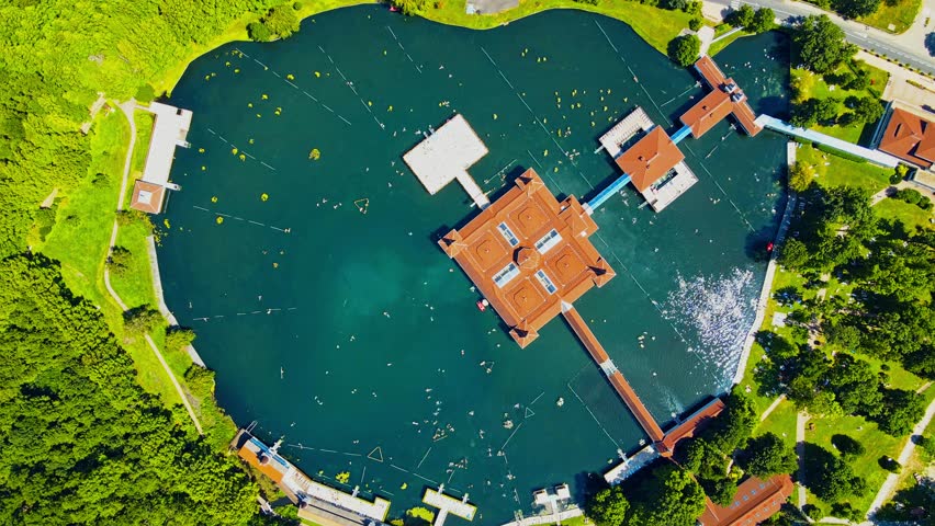 Aerial 4K drone footage of Thermal Lake of Hévíz in Hungary. Beautiful lake with thermal water. Trees grow around the lake. In the middle is a house, to which the galleries lead.