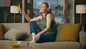 Excited lady dancing at couch place. Happy woman enjoying active music holding mobile phone at domestic interior. Smiling girl falling sofa feeling relaxed at lazy weekend. Carefree hipster at home - Powered by Shutterstock - Get 15% off with code: PIKWIZARD15