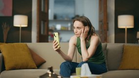 Crying lady talking smartphone on home sofa. Depressed woman speaking mobile phone at living room. Unhappy girl making cellphone video call sitting couch. Annoyed person complaining problems indoors