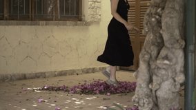 A spanish girl tramples a bed of purple and pink flowers in a rustic hallway house.