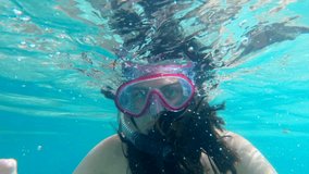 A young girl looks and greets to the camera while snorkeling on a sunny day.