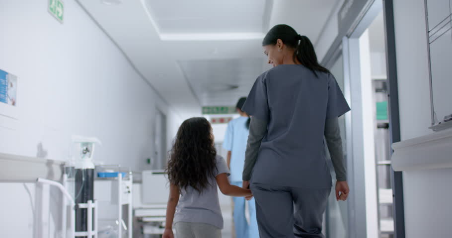 Diverse female nurse and child patient walking through corridor at hospital, in slow motion. Hospital, medicine and healthcare.