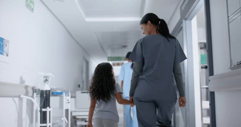 Diverse female nurse and child patient walking through corridor at hospital, in slow motion. Hospital, medicine and healthcare. Arkistovideo