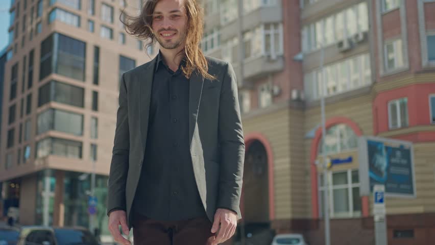 Portrait handsome man in coat looking at camera stand outdoors on background stairs. Sunlight at city street. Slow motion