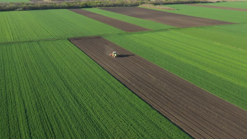 Above rotation view, orbit dolly move, of tractor as pulling mechanical seeder machine over arable field, soil, planting new cereal crop, corn, maize. Royalty-Free Stock Footage #1102825081