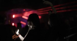 Two girls dancing on open space party with flashing lights and lasers. Friends standing one behind other. Out of focus crowd and dj stage in the background.