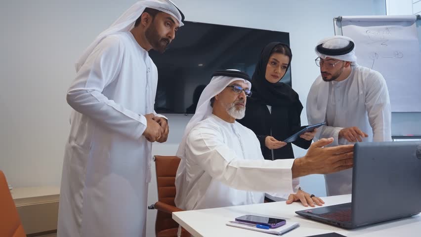 Business team at work in a office in Dubai. Locals from united arab emirates working on a new project wearing the formal traditional white outfit	 | Shutterstock HD Video #1102828319