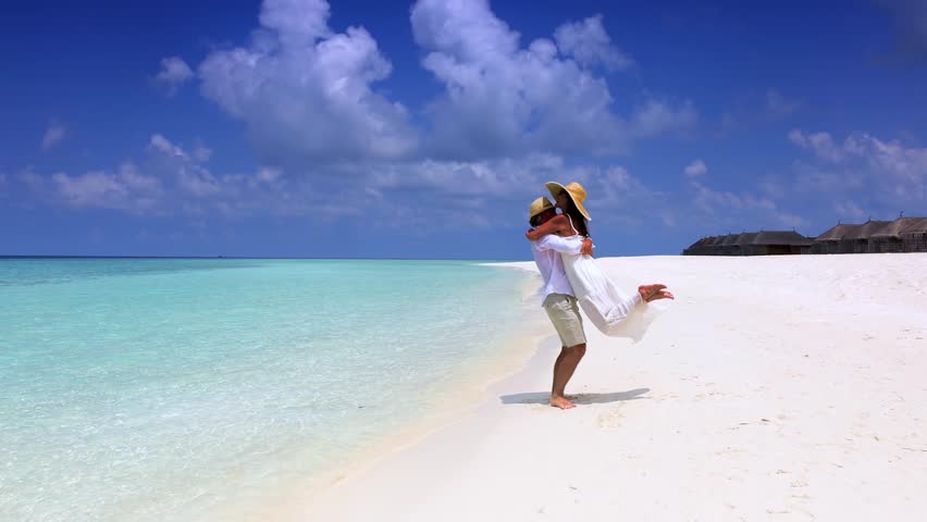 Happy couple in love is having fun and hugging on a sandbar with white sand and turquoise ocean