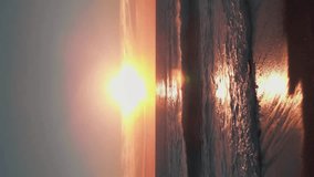 Golden pink sunset over sea water. Sun in colorful sky setting down over sea horizon. Sea waves crashing on beach. Vertical video. Beautiful seascape in evening dusk