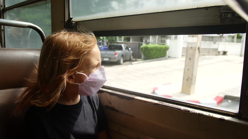 A girl in a medical mask rides in a bus with open windows