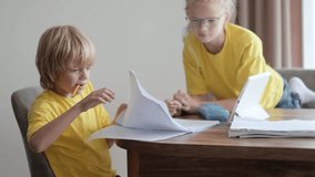 Sister helps little brother do school homework at home, Distance learning online education, boy and girl studying at home with digital tablet.