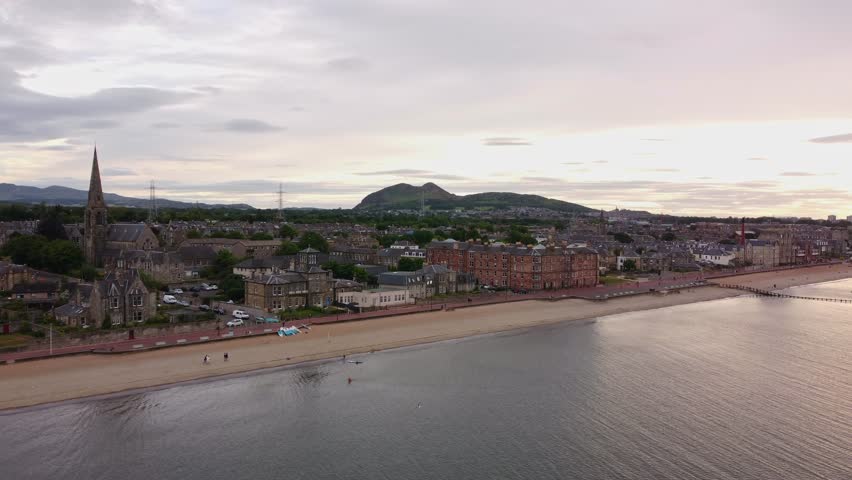 AERIAL: Portobello beach at sunset with people relaxing on the beach. Edinburgh, Scotland. Royalty-Free Stock Footage #1102835233