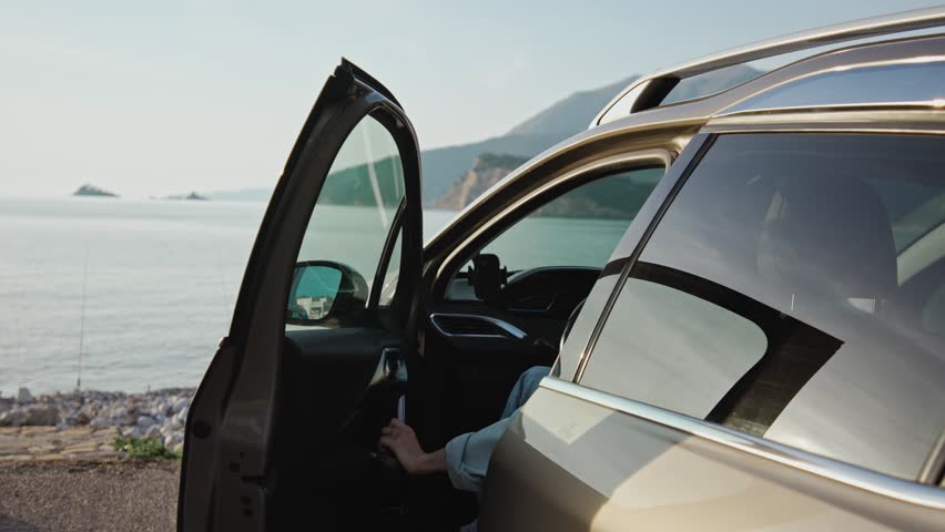 A young Caucasian woman gets out of her car parked by the sea and enjoys the beautiful sea view. Royalty-Free Stock Footage #1102835265