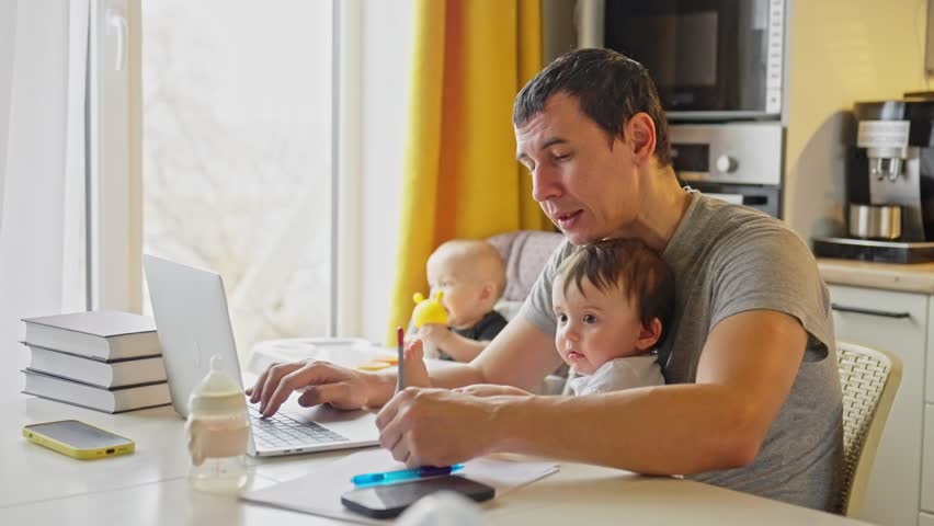 father working from home remotely with baby daughter in his arms. pandemic remote work business concept. father tries to work at home in kitchen fun, baby children interfere sitting on their hands Royalty-Free Stock Footage #1102838543
