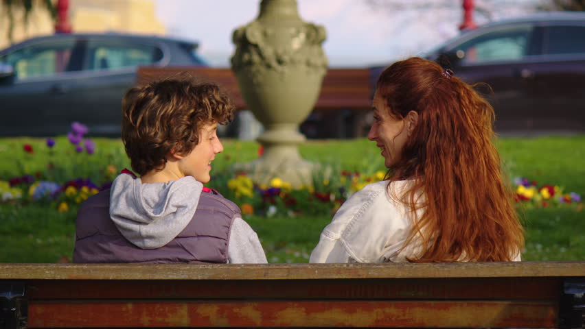 Caring mother talking to her son outdoor. A teenager discusses with his mom on a bench in the park. Raising a child by a mother, a serious conversation with a teenager in adolescence