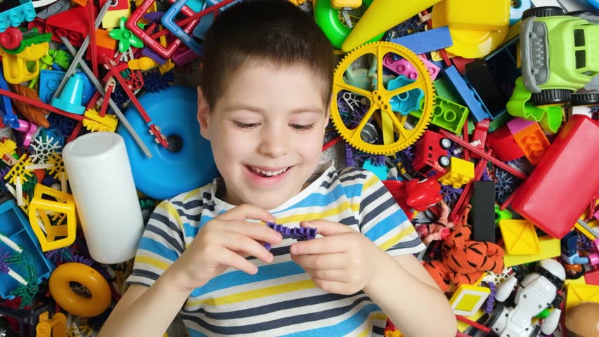 Cute little boy playing with toys lying among colorful toys on the floor, top view
