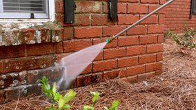 Pressure washer using water to clean a dirty brick wall on a house.